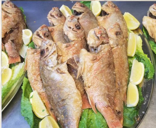 Platter of whole fried fish with lemon wedges and lettuce